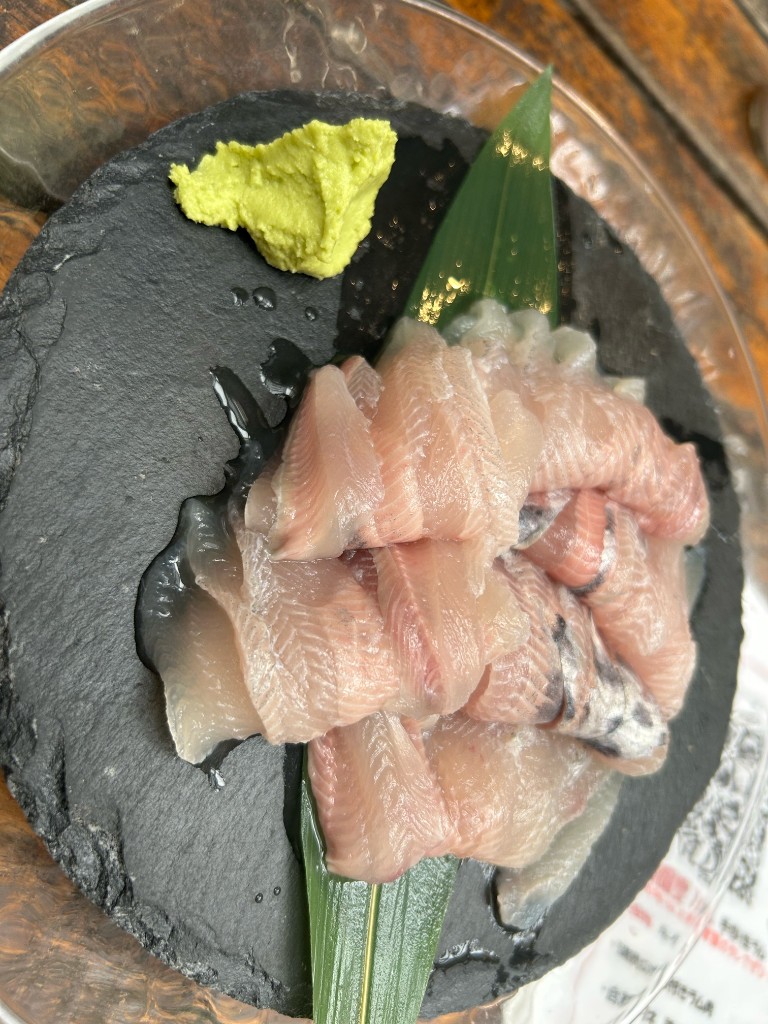 黒いスレートの皿に盛られた白身魚の刺身。左上に山わさび、笹の葉が添えられている（藍鱗の食堂）