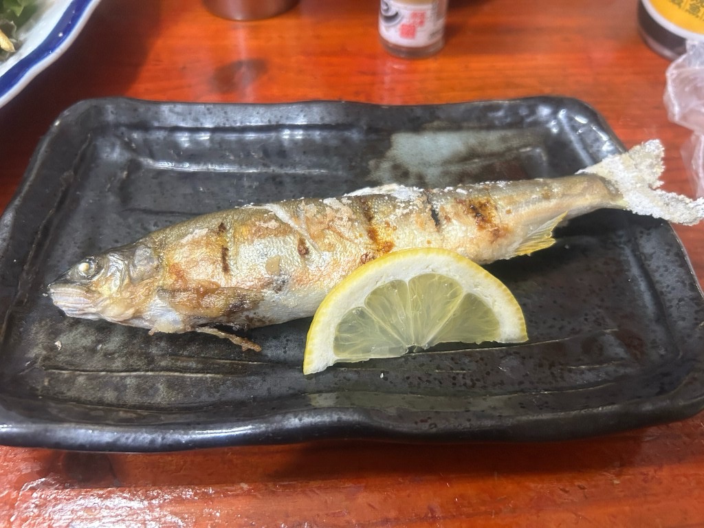 黒いプレートに盛られた丸ごと一本の焼き魚。レモンが添えられ、皮目に焦げ目がついた香ばしい仕上がり(居酒屋ふる里 麻生店)