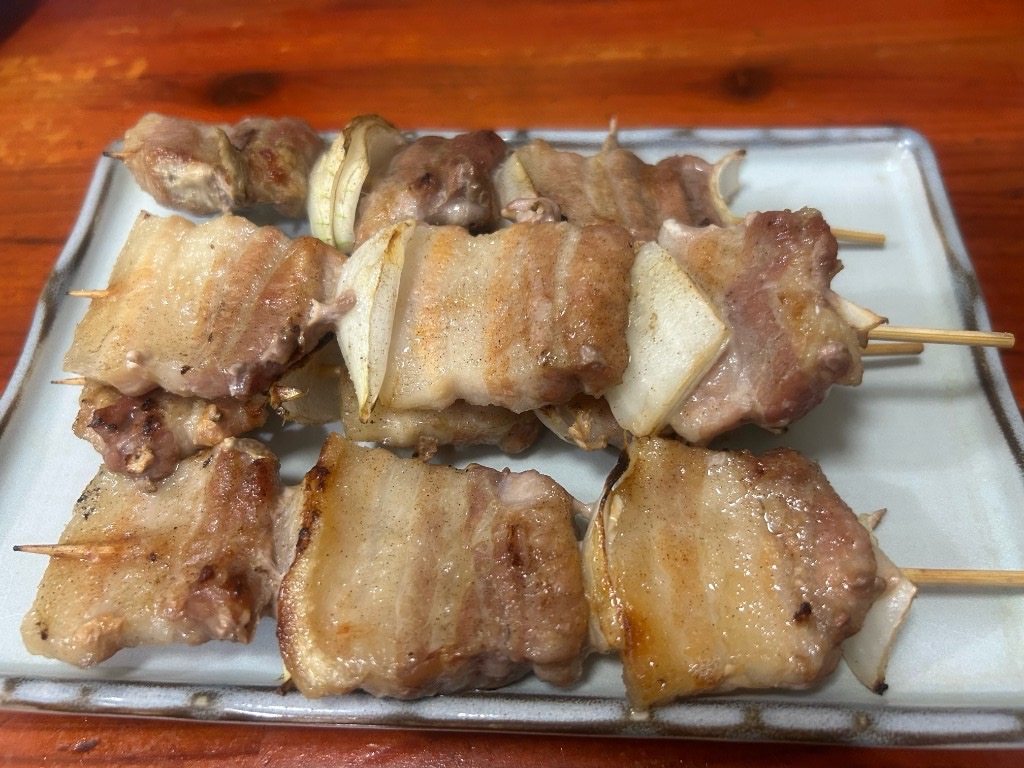 白い長方形の皿に並んだ8本の豚串。肉は厚切りで、軽く焦げ目がついた食べ応えのある仕上がり(居酒屋ふる里 麻生店)