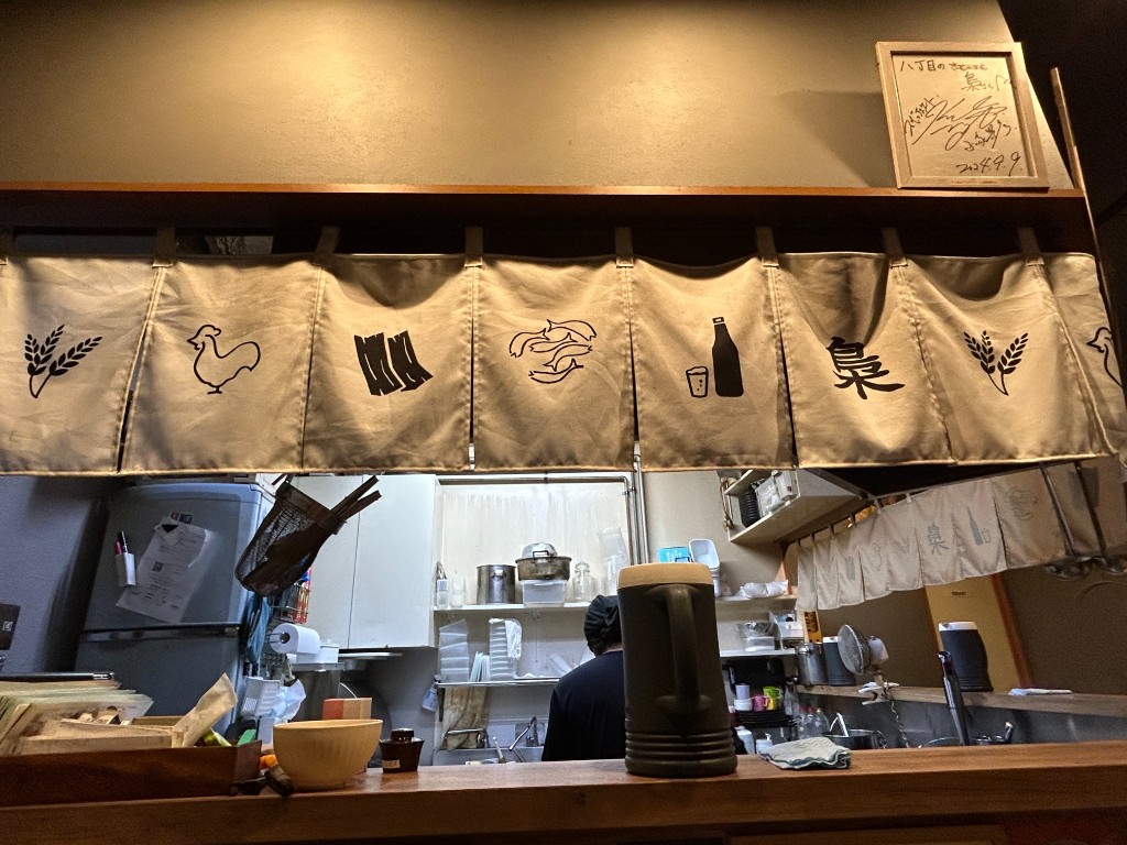 カウンター席から見た厨房。のれんに食材モチーフと「梟」の文字、色紙など
