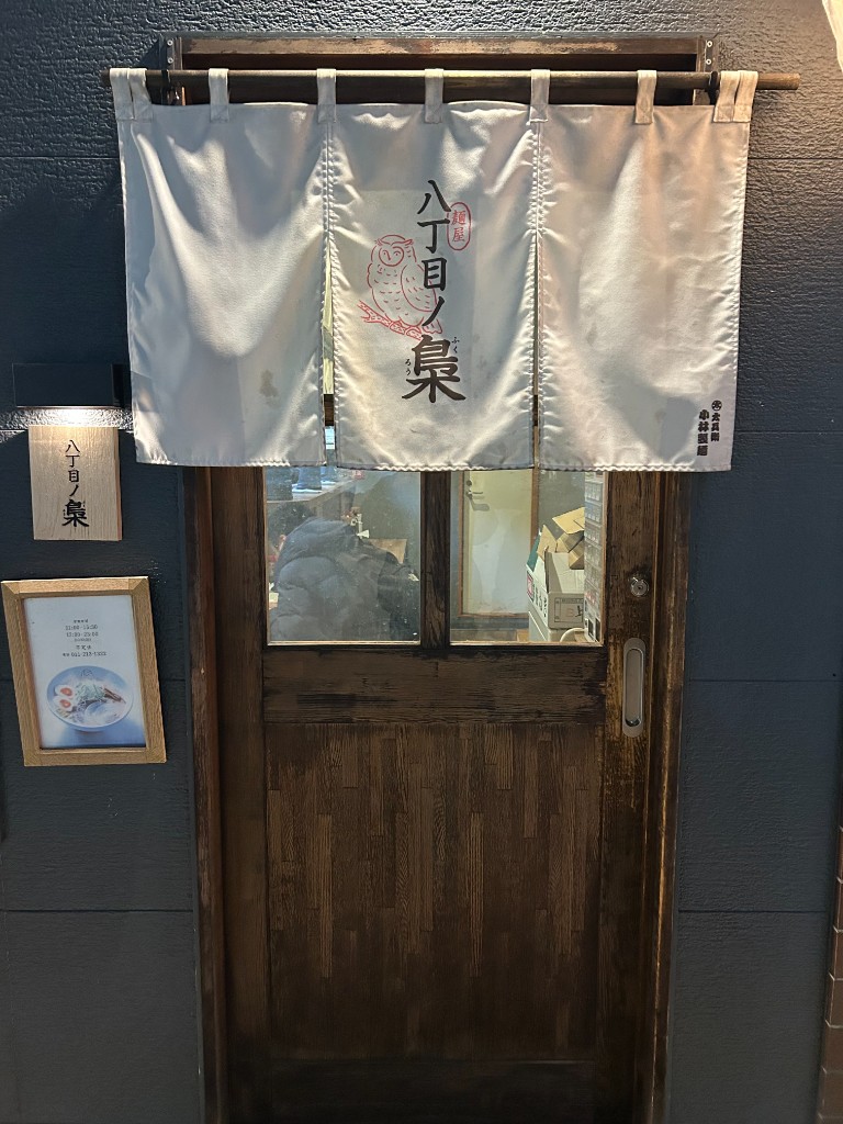昼の外観。白地の暖簾に梟のイラスト、「八丁目ノ梟」と麺屋の看板、木目の入口(麺屋 八丁目ノ梟)