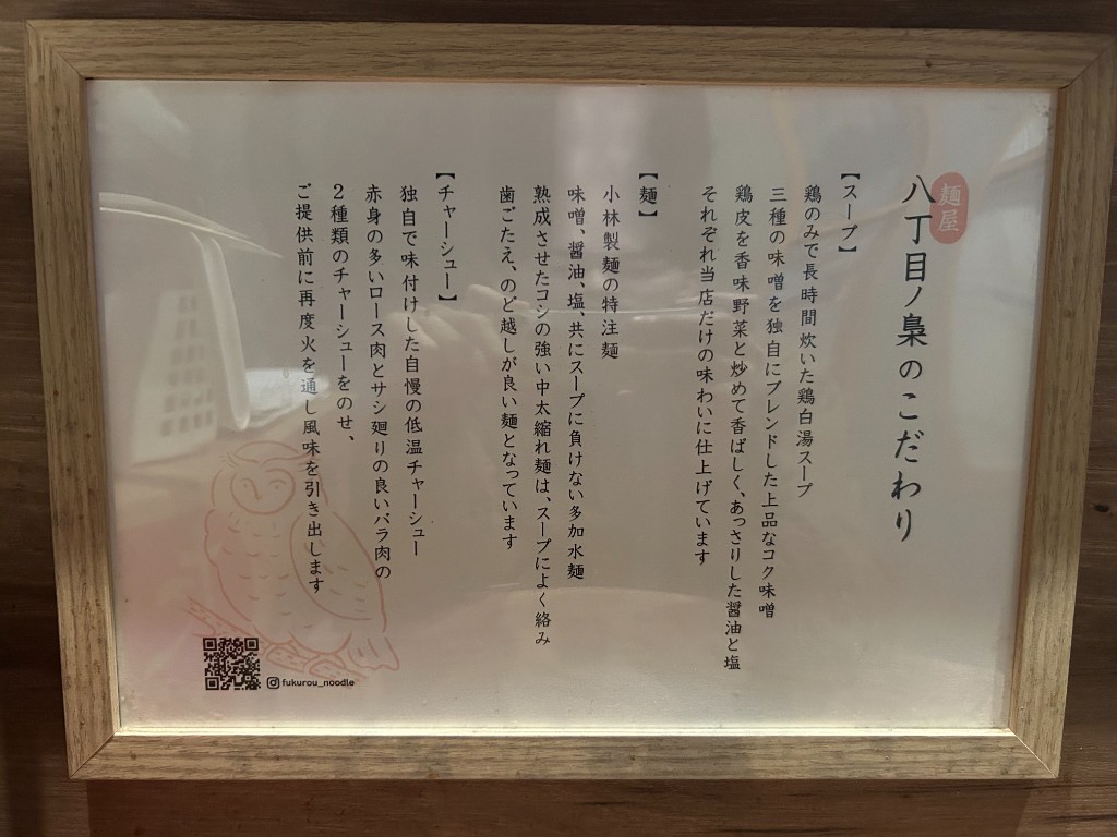 「麺屋 八丁目ノ梟のこだわり」と書かれた額装の案内板。梟のイラストとQR、SNS表記