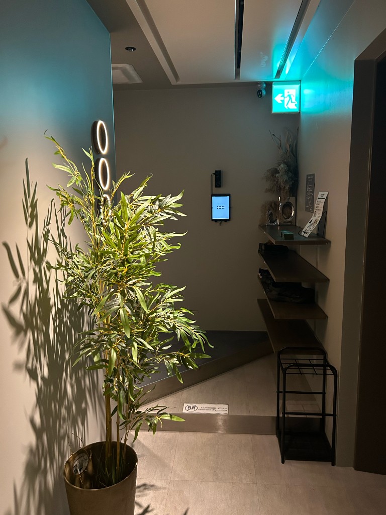 グリーンの鉢植えとリングライト、タブレットパネルが並ぶ入口。非日常へのゲートウェイ（SAUNA OOO SAPPORO）